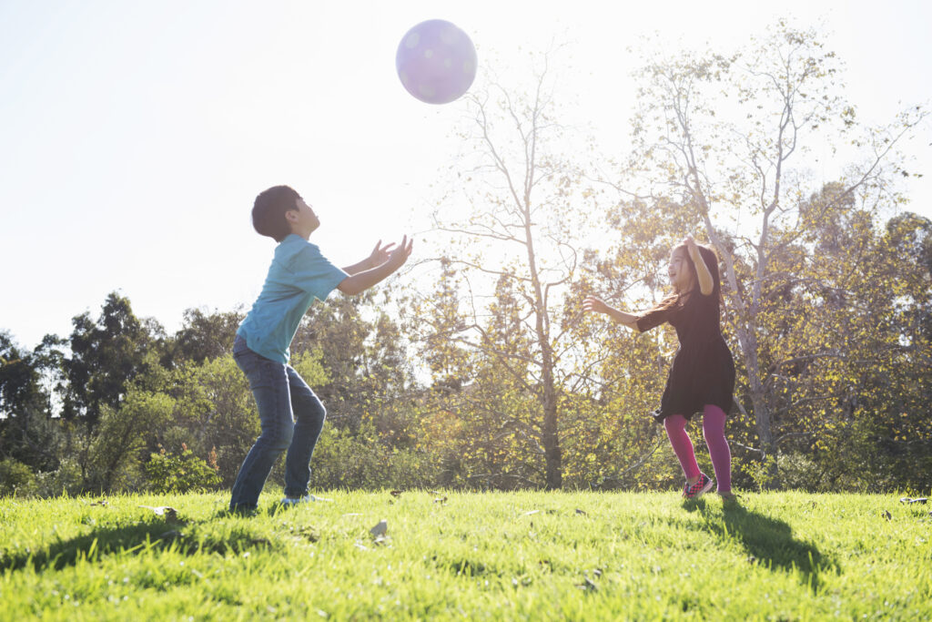 Twee kinderen spelen buiten en gooien een bal over naar elkaar